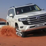 White Toyota Land Cruiser dune bashing and kicking up red sand on a Dubai desert safari.