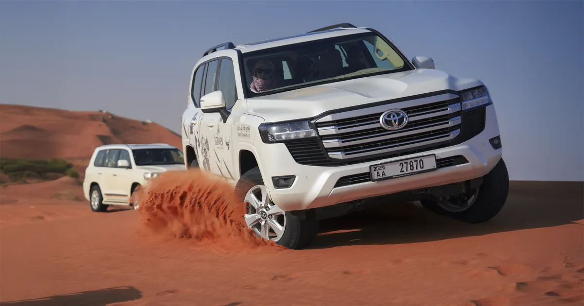 White Toyota Land Cruiser dune bashing and kicking up red sand on a Dubai desert safari.