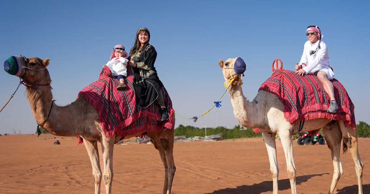 Mother and baby/child riding a decorated camel during a scenic and family-friendly camel ride experience with Trawey Tours in the Dubai desert.