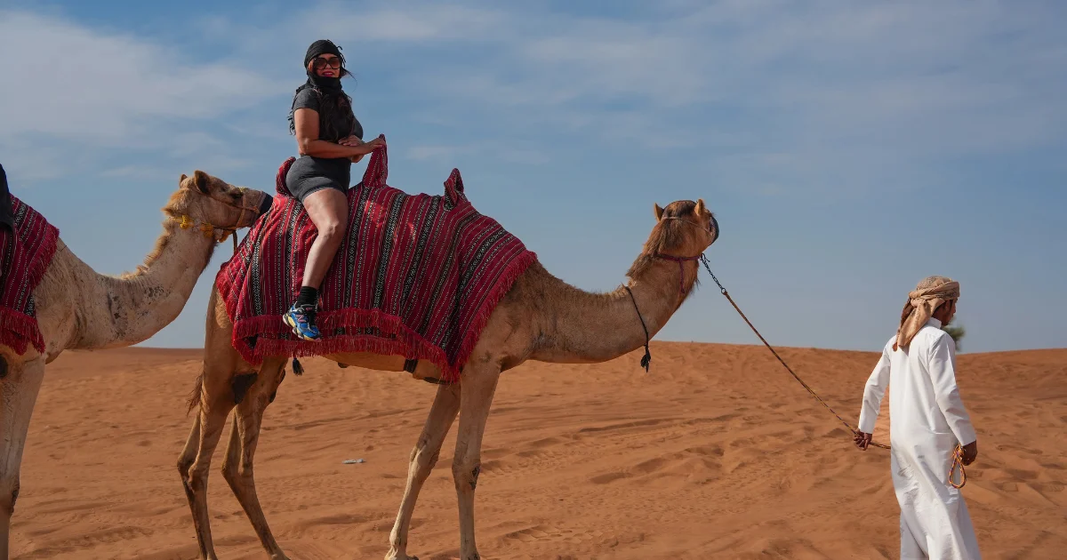 Woman riding a camel led by a local guide during Trawey’s Morning Desert Safari with Camel Ride in the Dubai desert.