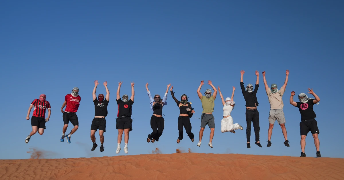 Happy group of tourists jumping on a sand dune celebrating UAE National Day Desert Safari with Trawey Tours.