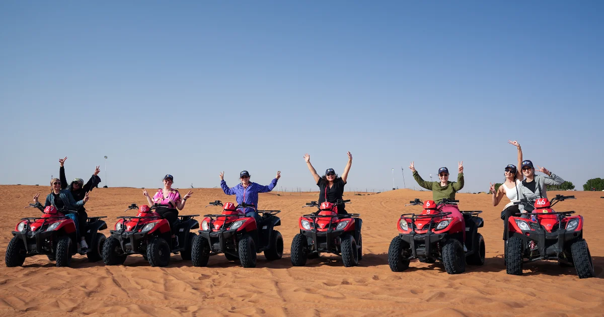 Group of happy women friends posing on red quad bikes during a thrilling desert safari adventure in Dubai with Trawey Tours.