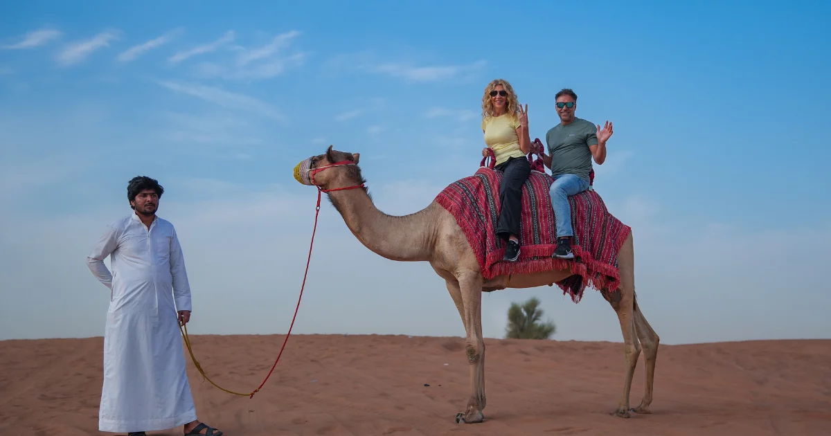 happy couple enjoys a gentle, ethical camel ride experience with Trawey Tours in the Dubai desert, led by a trained handler.