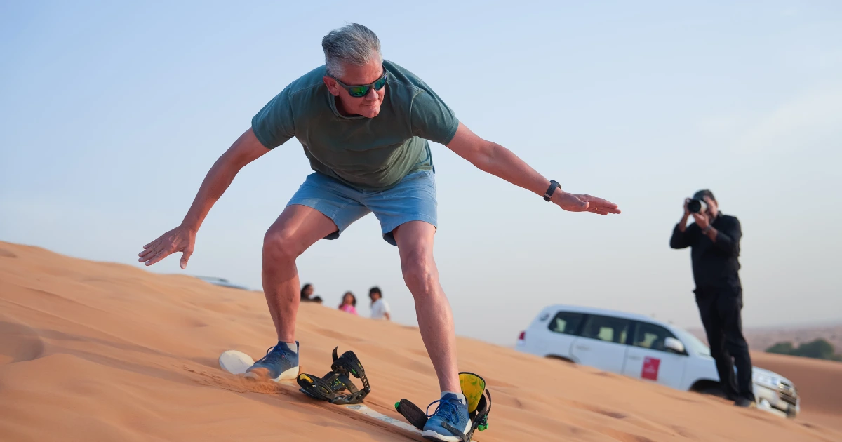 Active senior tourist trying a gentle sandboarding experience during a private desert safari with Trawey Tours in Dubai.