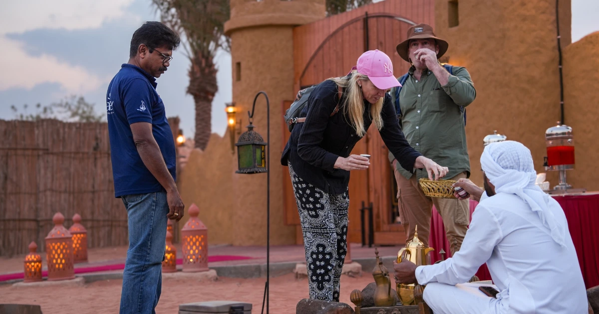 Tourists receiving a traditional Arabic coffee (Gahwa) and dates welcome at a Trawey desert safari camp entrance in Dubai.