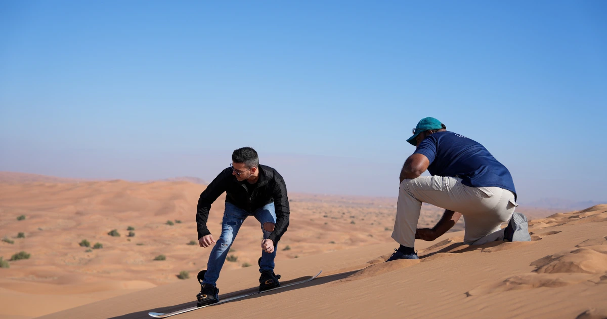 Beginner practicing the sideways sandboarding stance with a Trawey Tours guide on a Dubai dune.