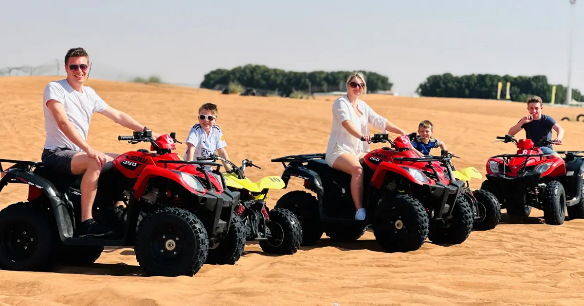 A family of four enjoying a quad biking adventure on sand dunes during a desert safari.